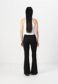 Black flared pants with a smooth texture, featuring a high waist and a fitted silhouette, paired with a white sleeveless top.