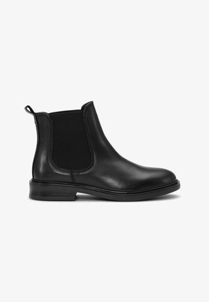 Bota Chelsea de cuero negro con paneles laterales elásticos, tira de sujeción en el talón, punta redondeada y tacón bajo apilado sobre fondo blanco.