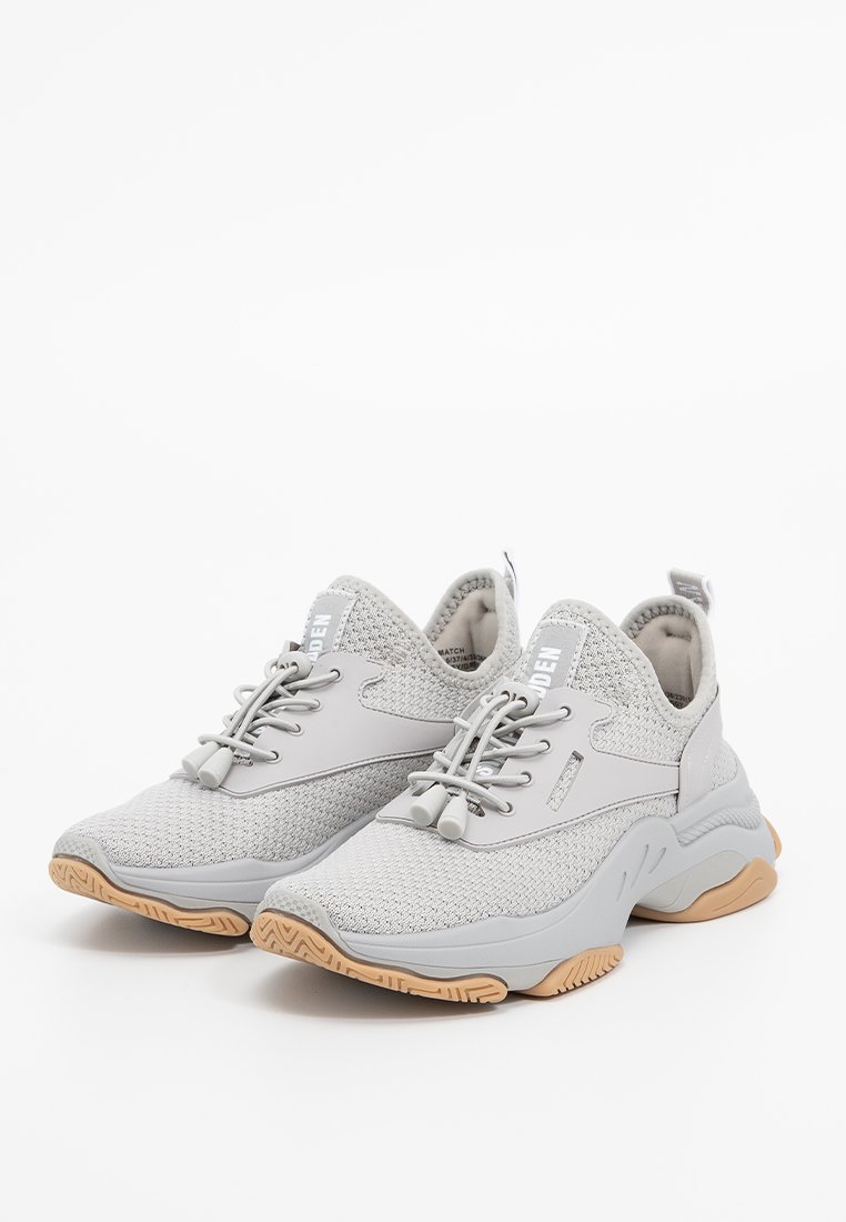 Zapatillas ligeras de color gris claro con parte superior de malla, cordones elásticos y suela de goma. Presentan una puntera redondeada y acentos texturizados.
