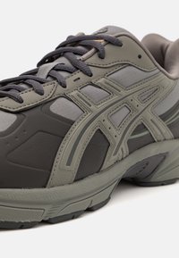 Šedá a černá sportovní obuv s texturovanou gumovou podrážkou, vrchní část z látky a syntetického materiálu, a tmavě šedé tkaničky svázané do mašle.