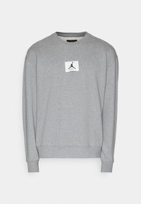 Sweat-shirt gris à manches longues avec col rond, orné d'un patch logo Jumpman noir et blanc centré sur la poitrine.
