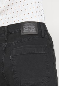 Vaqueros de mezclilla negra con diseño de pierna recta. Presentan una etiqueta de cuero con la marca y un solo bolsillo trasero. Tejido texturizado con costuras mínimas.