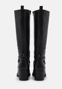 Botas de cuero negro hasta la rodilla con una textura suave, un tacón cuadrado y correas decorativas con acentos metálicos. Cierre de cremallera en la parte posterior.