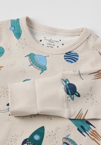Beige Langarmshirt mit bunten Weltraummustern, darunter Raketen und Planeten. Weicher Baumwollstoff mit geripptem Ausschnitt.