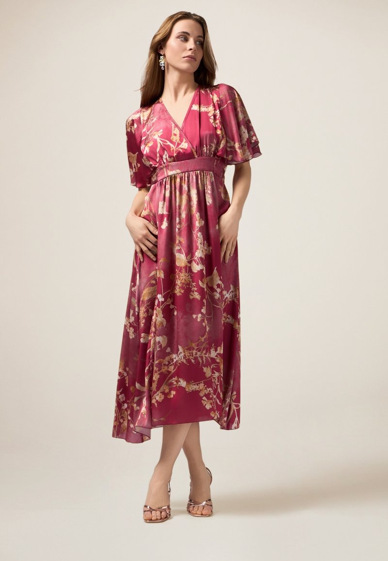 Un vestido largo y fluido en un rico burdeos con patrones florales, mangas cortas y una cintura ajustada. Combinado con sandalias con tiras.