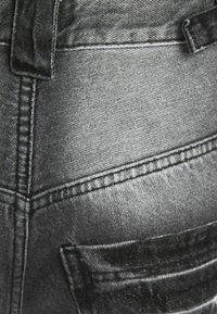 Närbild av urblekta svarta denimjeans som visar ficka, bältesslinga och detaljerad sömnad.