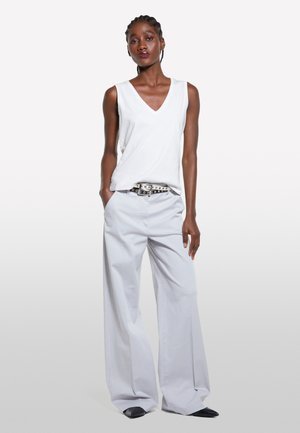 Haut sans manches blanc en V associé à un pantalon large gris clair. Ceinture noire avec des accessoires en métal argenté. Texture de tissu lisse.