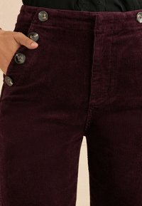 Bordo kadrovane hlače s vertikalnom rebrastom teksturom, s pet ukrasnih dugmadi sprijeda i visokim strukom.