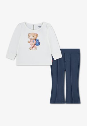 Witte longsleeve met teddybeer in een roze outfit en blauwe rugzak, gecombineerd met donkerblauwe, getextureerde broek.