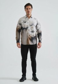 Chemise à boutons florale avec un motif de fleurs blanches et beiges rehaussé d'accents noirs, fabriquée en tissu doux ; associée à un jean noir et des baskets.