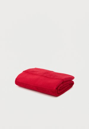 Serviette de bain rouge pliée avec une bordure texturée posée sur une surface blanche unie.