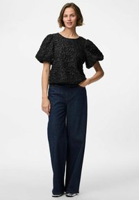 Svart strukturerad topp med puffärmar, kombinerad med vida mörkblå jeans som har en klassisk rund halsringning.