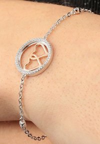 Bracciale in argento caratterizzato da un pendente circolare con forme di cuori intrecciati, circondato da piccoli cristalli trasparenti lungo i bordi. Catena regolabile.