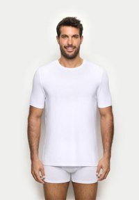 T-shirt bianco a maniche corte realizzato in tessuto liscio, con collo rotondo classico e silhouette aderente. Abbinato a slip bianchi.