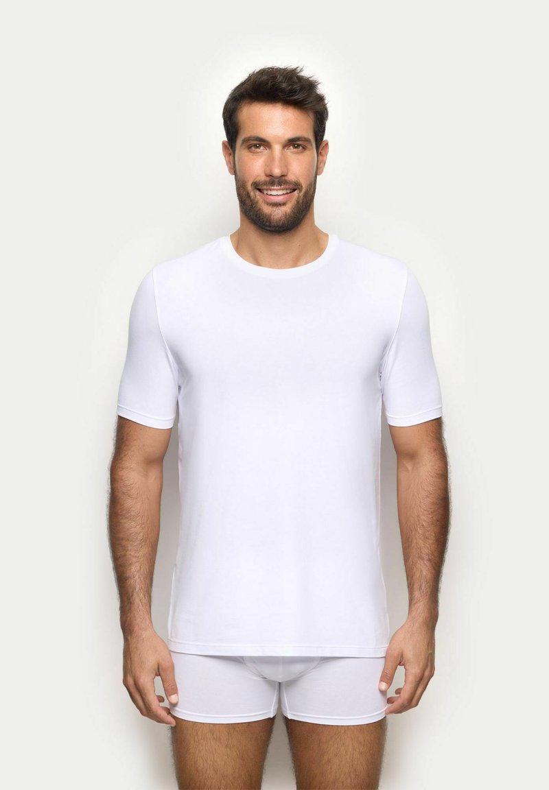 T-shirt bianco a maniche corte realizzato in tessuto liscio, con collo rotondo classico e silhouette aderente. Abbinato a slip bianchi.
