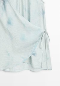 Jupe portefeuille tie and dye bleu clair avec liens latéraux créant un effet drapé à couches dans un tissu doux et texturé.