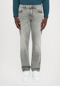 Grå denimjeans med avslappnad passform, fem fickor och blekt utseende. I kombination med vita sneakers mot en enfärgad bakgrund.