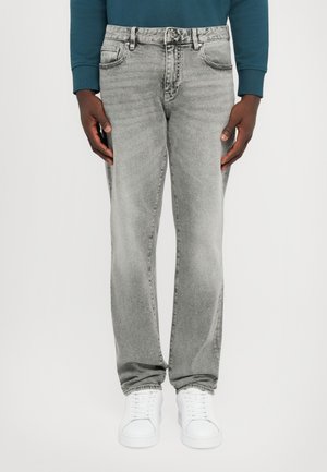 Grå denim jeans med en avslappet passform, fem lommer og falmet tekstur. Kombinert med hvite sneakers på en ensfarget bakgrunn.
