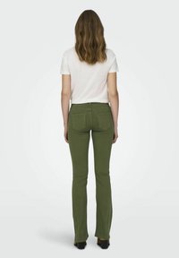 Jeans évasés verts avec cinq poches, taille haute et texture lisse, associés à un t-shirt blanc uni à manches courtes.