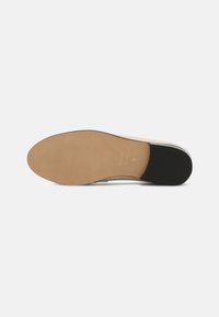 Suola piatta di scarpa con una superficie in gomma beige, caratterizzata da un motivo testurizzato e un accento nero nel tallone. Design a doppio materiale.