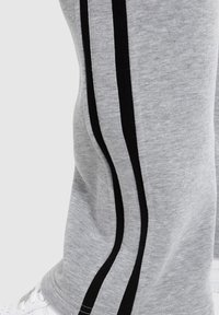 Graue Sweatpants mit einer weichen Textur, die an den Seiten zwei schwarze vertikale Streifen aufweisen. Getragen mit weißen Turnschuhen.