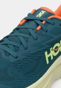 Παπούτσι τρεξίματος σε τυρκουάζ χρώμα με υφασμάτινο επάνω μέρος με υφή, πορτοκαλί κορδόνια και κίτρινο λογότυπο της μάρκας. Ελαφρύ ενδιάμεσο πέλμα με κυρτό σχήμα για άνεση.