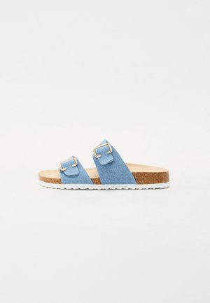 Blue denim two-strap slide sandals with gold buckles, a cork footbed, and a white rubber sole. Flat design with a casual aesthetic.
