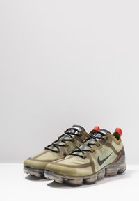 Sneaker Nike VaporMax verdi e nere presentano una tomaia in mesh texture, un distintivo motivo camouflage e una suola trasparente con ammortizzazione ad aria e dettagli rossi.
