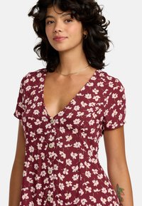 Robe bordeaux à manches courtes, ornée d'un motif floral rose et blanc. Elle a un col en V et des boutons décoratifs sur le devant.