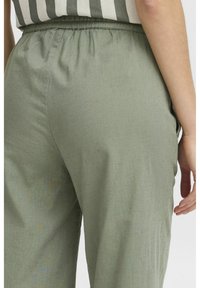 Pantaloni leggeri di colore verde chiaro con una cintura elastica. Il tessuto presenta una trama sottile, con tasche laterali in vista.