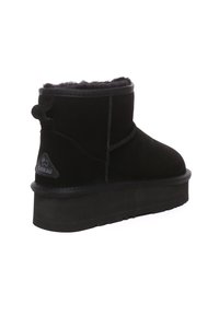 Black suede ankle boot with a soft interior lining, chunky rubber sole, and a decorative back pull tab. Features a logo patch on the side.