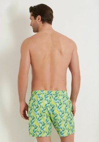 Miestenské plavky v jasne žltej farbe s tropickým listovým vzorom v zelenej a modrej farbe, so elastickým pásom a voľným strihom.