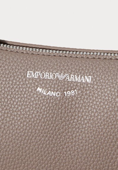 Ruskean tekstuurin omaava nahka, jossa on hopeinen Emporio Armani -logo ja "MILANO 1981" -yksityiskohta. Vetoketjulla suljettava yläosa.