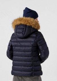 Giacca piumino blu navy con cappuccio in ecopelliccia staccabile. Design trapuntato verticale, spessore medio e texture liscia in nylon.