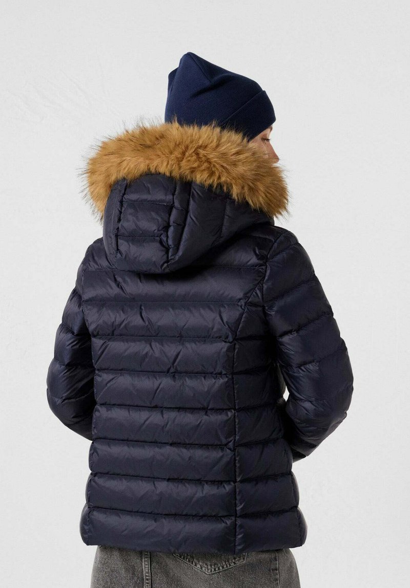 Giacca piumino blu navy con cappuccio in ecopelliccia staccabile. Design trapuntato verticale, spessore medio e texture liscia in nylon.