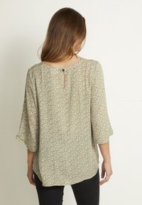 Hellgrüne Bluse mit Blumenmuster, Dreiviertelärmeln, Keyhole-Rückendetail und weichem, strukturiertem Stoff.
