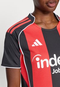 Raudonas ir juodas sportinis marškinėliai su trumpomis rankovėmis, su baltais akcentais, Adidas logotipu ir "indee" ženklu balta spalva priekyje.