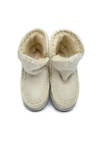 Zapatillas color crema con un interior suave y texturizado, que presentan un cuello doblado y costuras visibles a lo largo de los bordes.