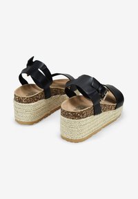 Sandalias de plataforma negras con correas anchas, que cuentan con una suela de yute trenzado y una entresuela similar al corcho. Detalle de hebilla en la correa, plantilla texturizada.