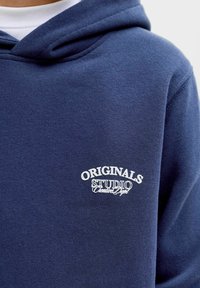 Námořnický svetr s kapucí, měkkou texturou a vyšívaným logem s nápisem "ORIGINALS STUDIO" v bílé barvě. Standardní střih.