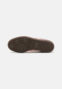 Sola de sapato com um design em borracha moldada, apresentando uma superfície texturizada castanha, padrões circulares e um logótipo "adidas" perto do calcanhar.