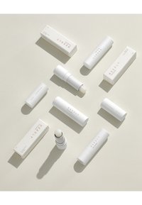 Tubes et boîtes de baume à lèvres cylindriques blancs, au design minimaliste avec un texte simple. Finitions douces et ombres légères sur un fond neutre.