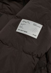 Donsjack in donkerbruin, met een gequilt ontwerp, een soepele textuur en een zijlabel met bedrukte details in het wit.