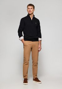Mörkblå tröja med dragkedja över en vit skjorta, kombinerad med beige chinos och bruna sneakers. Outfiten har en slim-fit design.