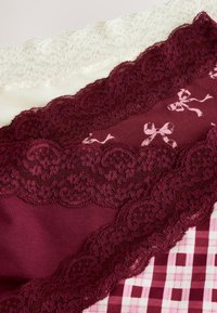 Capas de tela con encaje en blanco y marrón granate, con patrones florales y de lazos. Texturas suaves y diseños variados de encaje son prominentes.