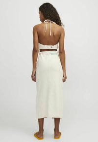 Falda color crema con un diseño largo y recto, bolsillos laterales y costuras rosas en contraste. La parte superior tipo halter cuenta con un cierre de lazo y una banda.