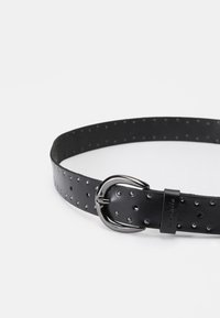 Cinto de couro negro com tachas prateadas, uma fivela metálica redonda e textura suave. O design inclui furos espaçados uniformemente ao longo do comprimento.