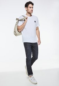 Vit bomullströja med en liten logotyp, mörka jeans och vita sneakers. Bär en ljusgrå kanvasväska. Avslappnad outfit.