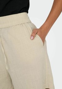 Shorts en lin beige avec une taille élastique et une poche latérale, présentant un motif texturé subtil et une coupe ample pour le confort.