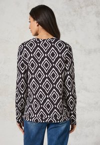 Schwarzes und weißes gemustertes langärmliges Oberteil mit Rautenformen, rundem Halsausschnitt und lockerer Passform, kombiniert mit blauen Jeans.